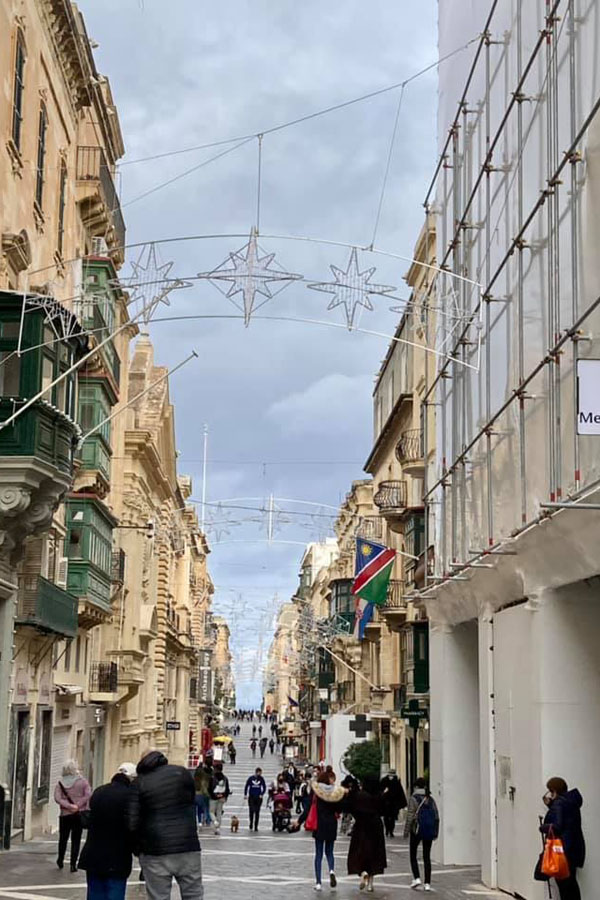 Maltese people wearing winter coats on a narrow street in Valletta, Malta, at 60 degrees.