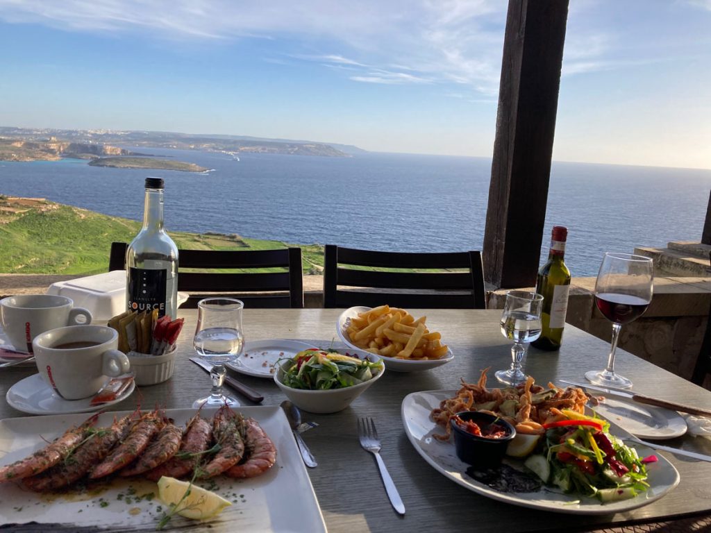 Appealing food on a table with a view of the islands of Comino and Malta