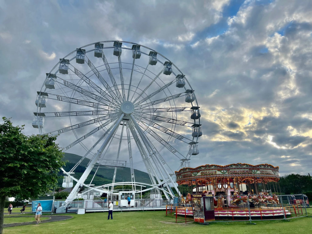 A Ferris Wheel with a carousel in the foreground, with clouds in the background.