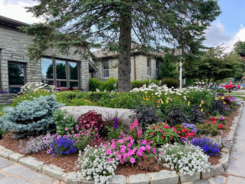 Colorful flowers bloom in a flower bed in front of attractive stone buildings.
