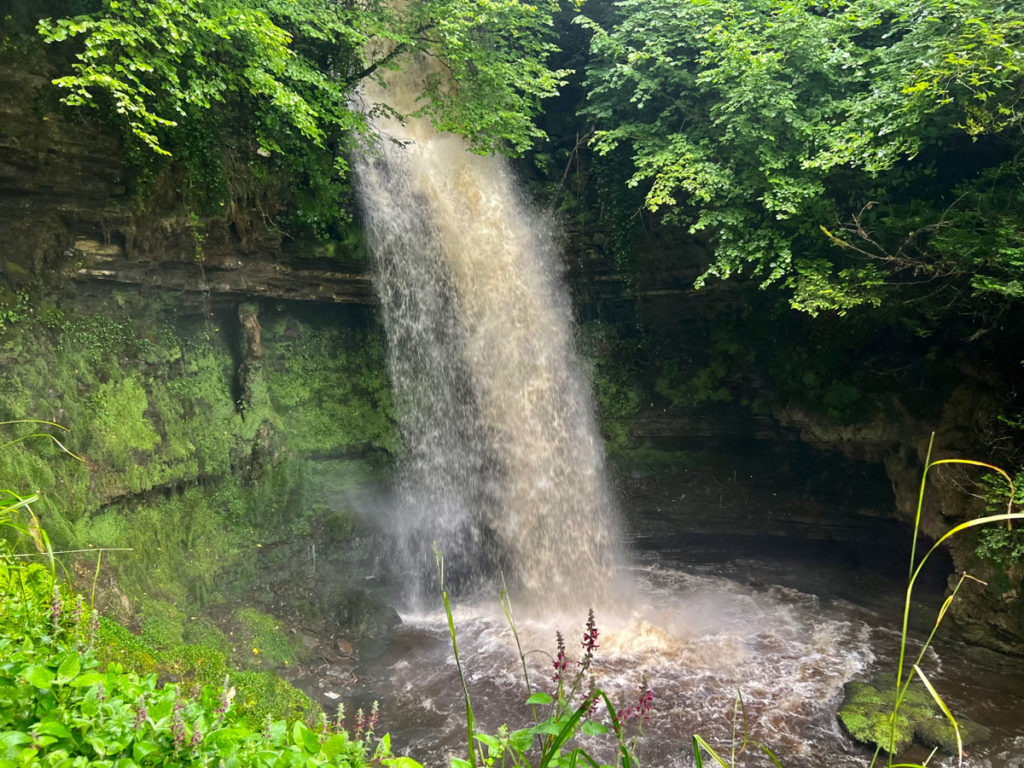 A 50-foot-tall waterfall cascades into a natural pool with moss-covered rock walls.