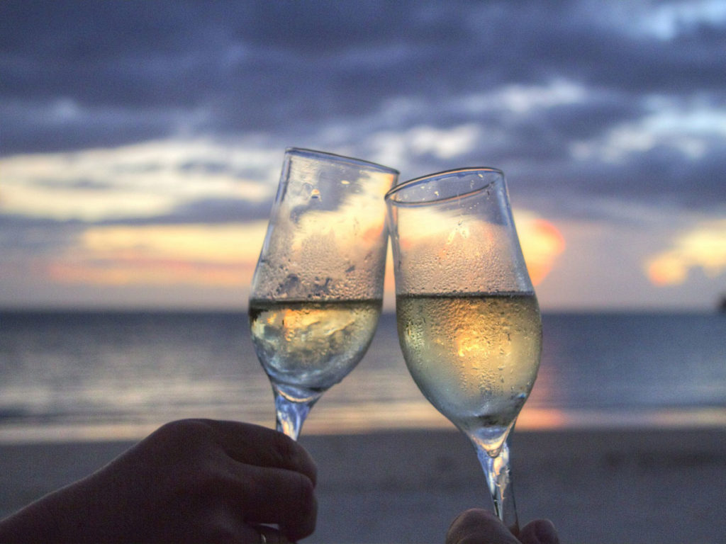 Two cold glasses of white wine in front of a beach sunset.