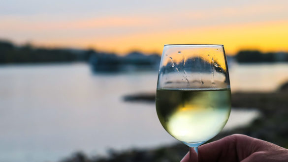 White wine in a glass, against an artistically blurred background of a sunset over water