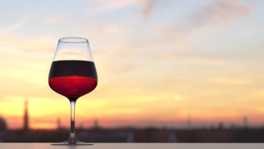 A glass of red wine on the left, with a sunset in the background