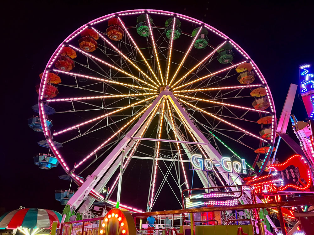 Amusement park rides including a Ferris wheel are lit colorfully at night.