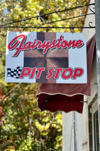A sign with text reading "Fairystone Pit Stop" over a graphic of a staurolite shaped like a Maltese cross.